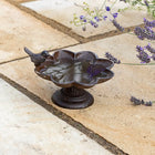 Decorative bird bath with a bird on a stone patio with lavender flowers.
