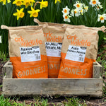 Three large orange bags of Ark Wildlife bird food placed in a wooden tray with a garden in the background.