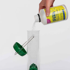 Person pouring a liquid from a bottle labeled 'Feeder Fresh' into a green bird feeder.