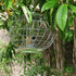 Metallic caged bird feeder hanging among green leaves