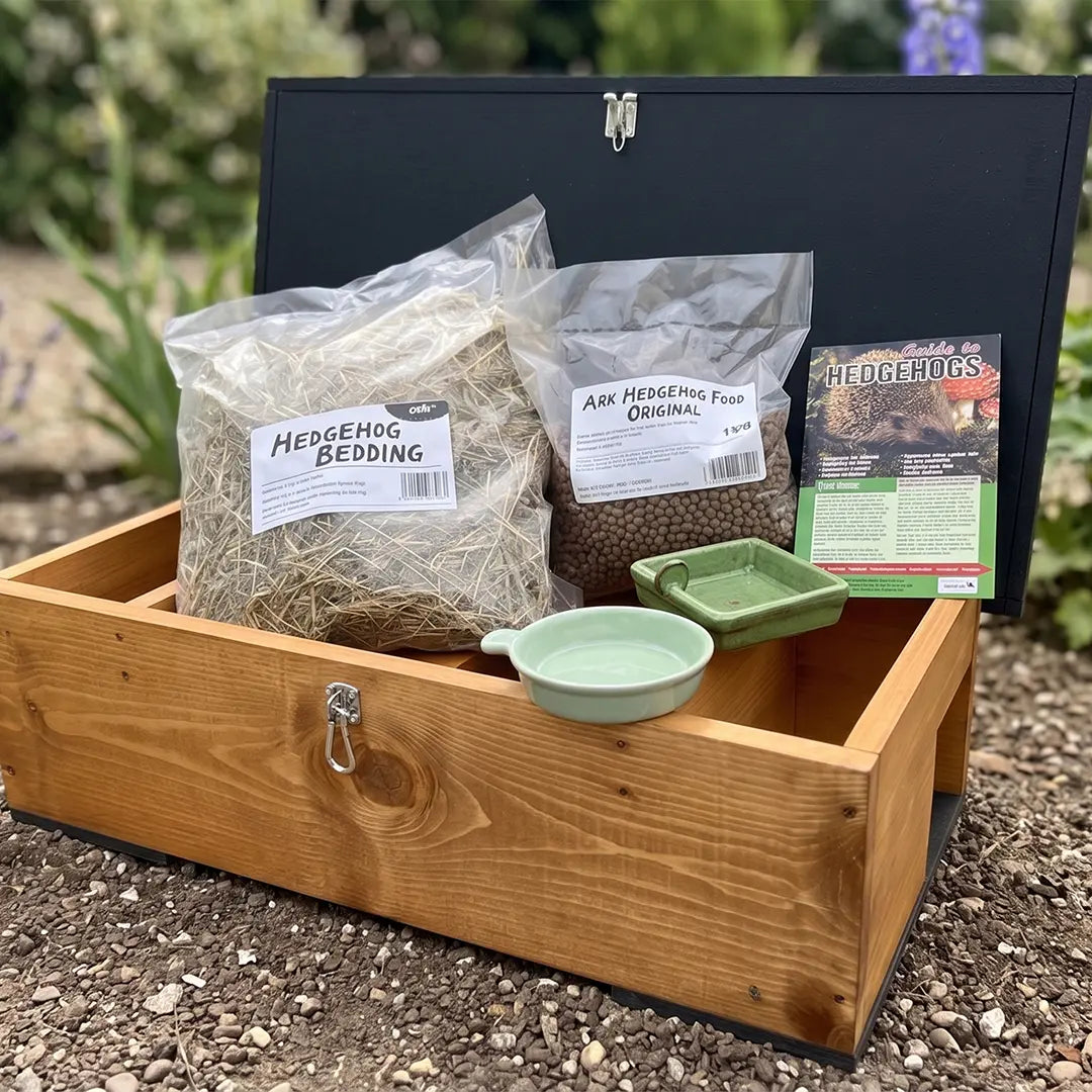 Wooden hedgehog house including bedding, food, and a bowl on a natural background.