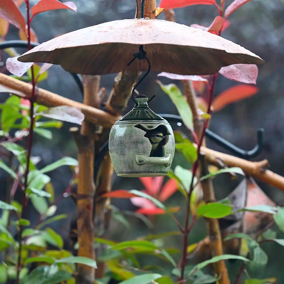 Decorative metal squirrel baffle bird feeder hanging from a branch with leaves in the background