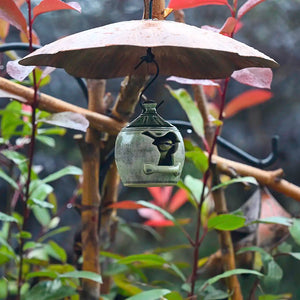 Decorative metal squirrel baffle bird feeder hanging from a branch with leaves in the background