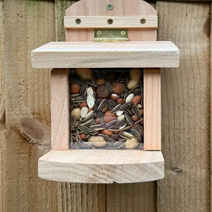 Wooden squirrel feeder with seeds and nuts on a fence