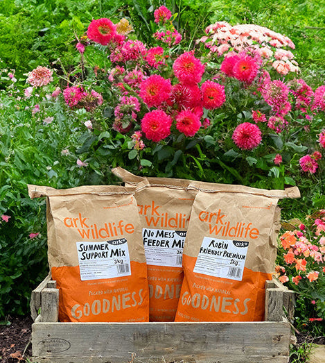 Three bags of ark wildlife products in a wooden crate with flowers in the background